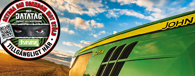John Deere 6215R traktor i närbild med tydlig logotyp och grönt motorhuv, bredvid en Datatag-skylt som uppmanar till stöldskydd för maskiner.