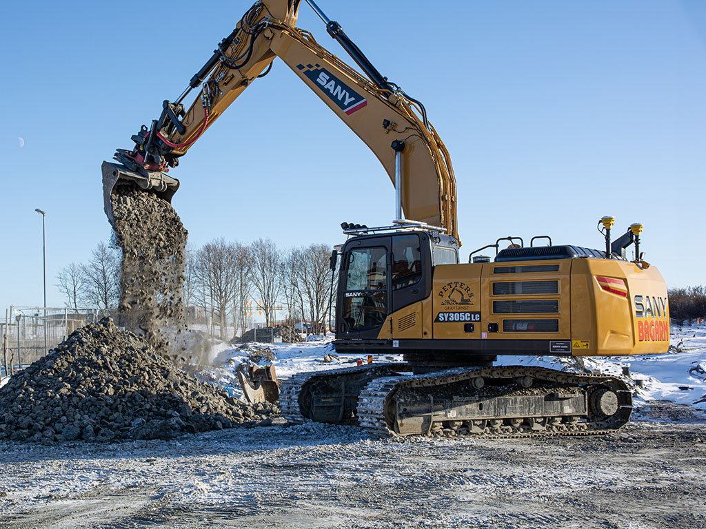 SANY bandgrävare SY305 lastar stenmaterial på en snötäckt arbetsplats under vinterförhållanden.
