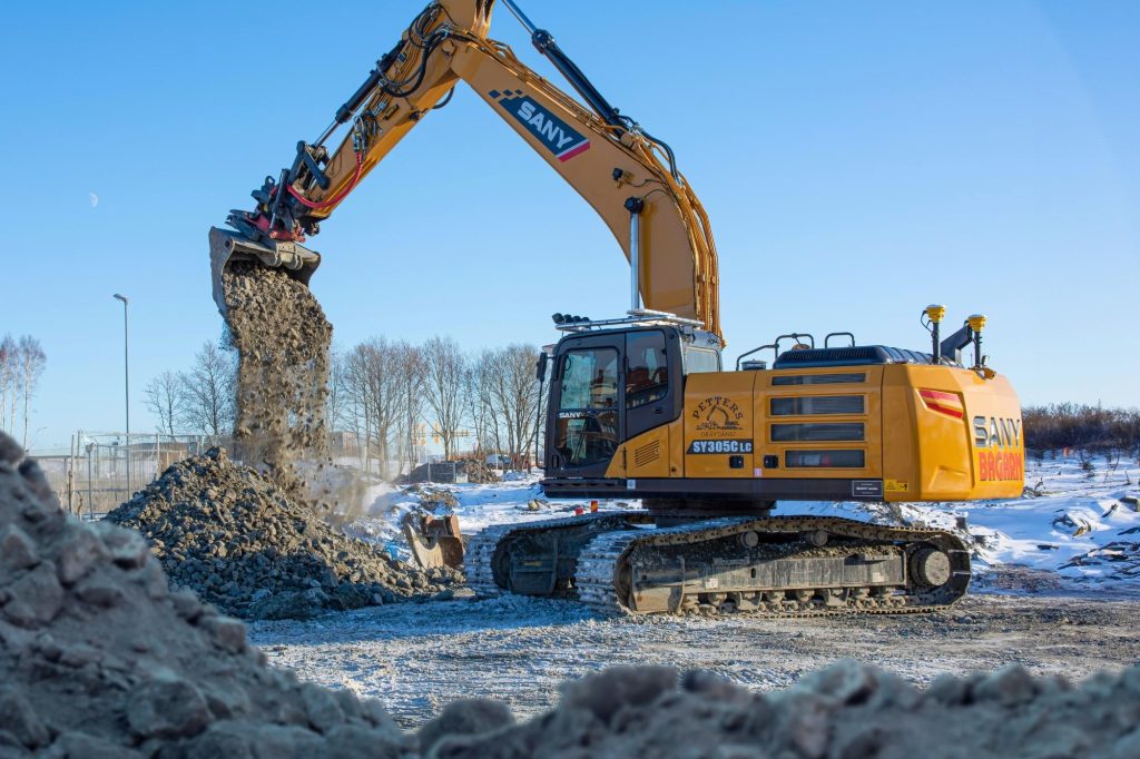 Bandgrävare SANY SY305 lastar stenmaterial på en byggarbetsplats under vinterförhållanden.