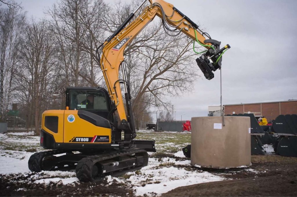 SANY SY80U kompaktgrävare lyfter betongbrunn på arbetsplats med snö, utrustad med tiltrotator och hydraulik.